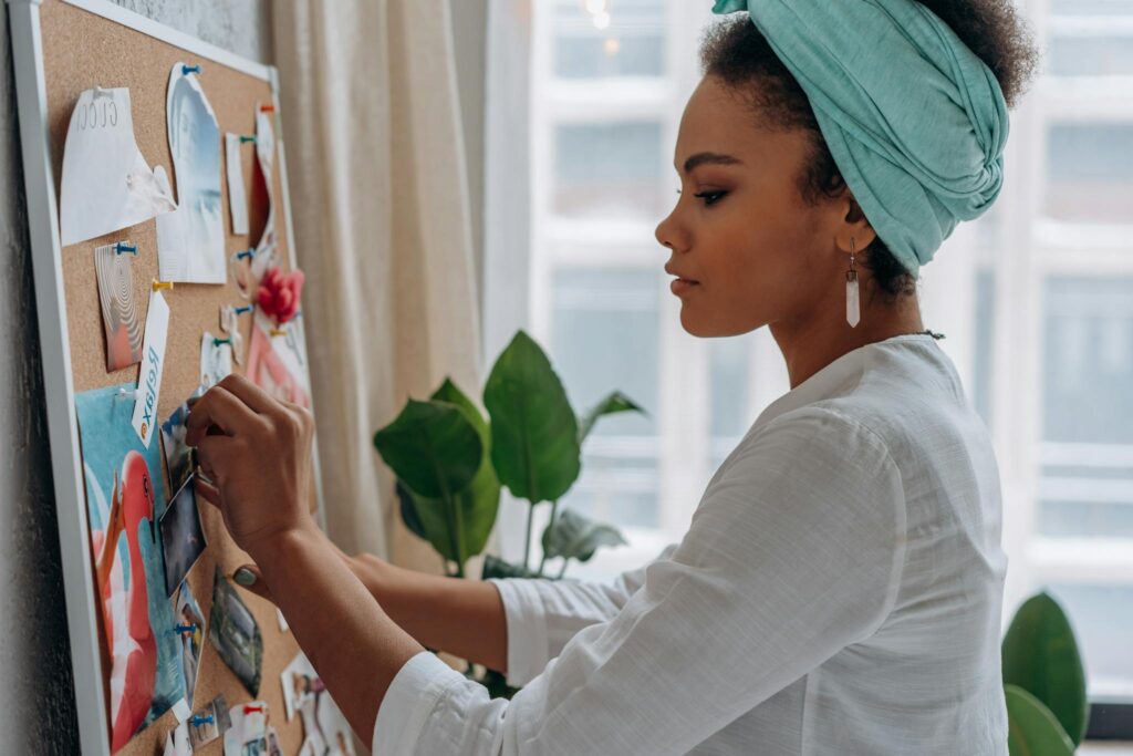 Woman creating a vision board with images in a stylish home setting, showcasing creativity and focus.